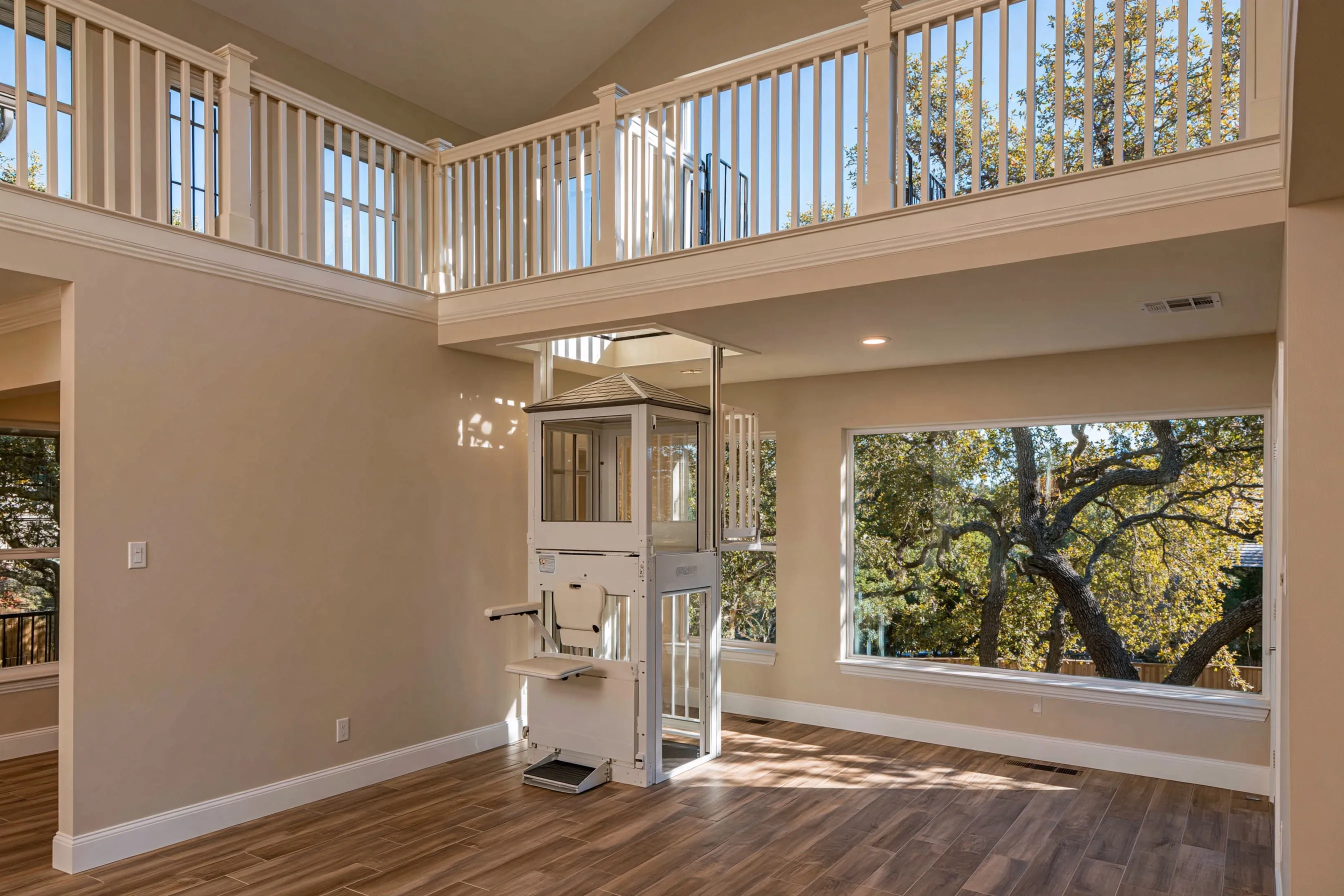 Compact one-seat through-floor lift in a family room corner, rising through a framed opening into an open loft with a railing